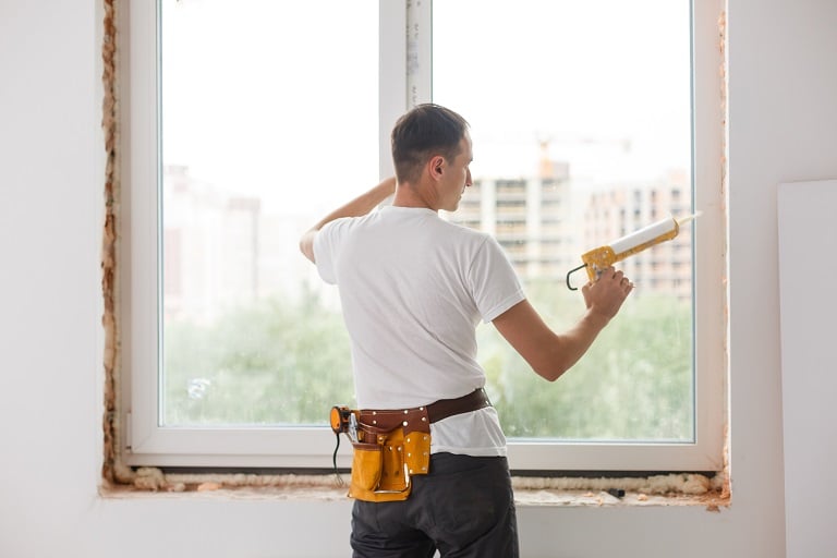 A man contractor caulks a new window frame