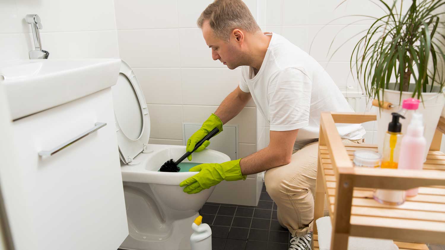 A man cleaning a toilet with a brush.