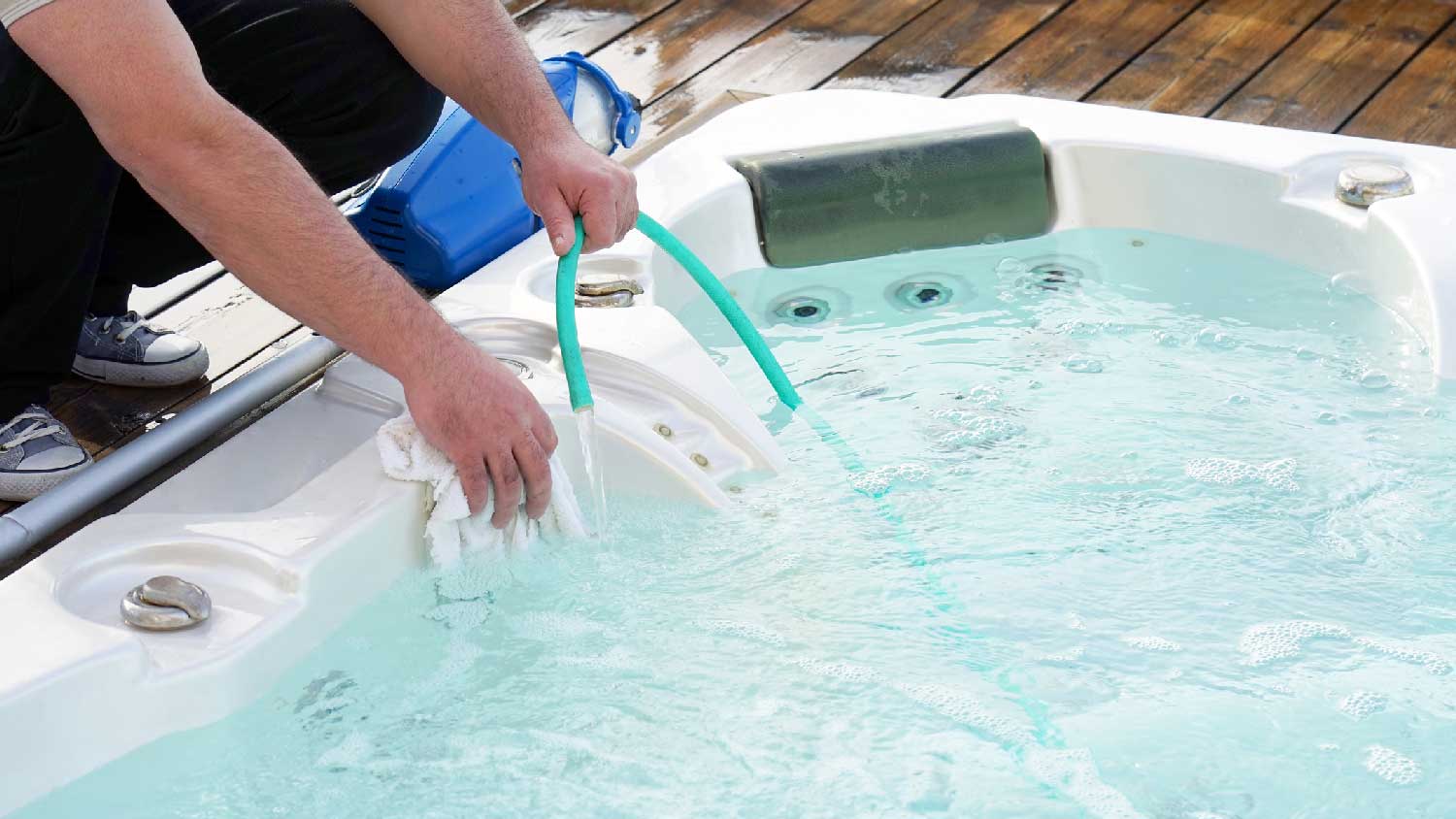 A man cleaning a hot tub with a hose and a rag