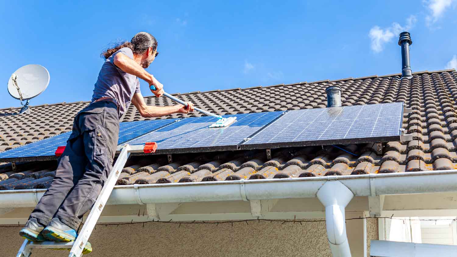 A man cleaning solar panels on a house’s roof