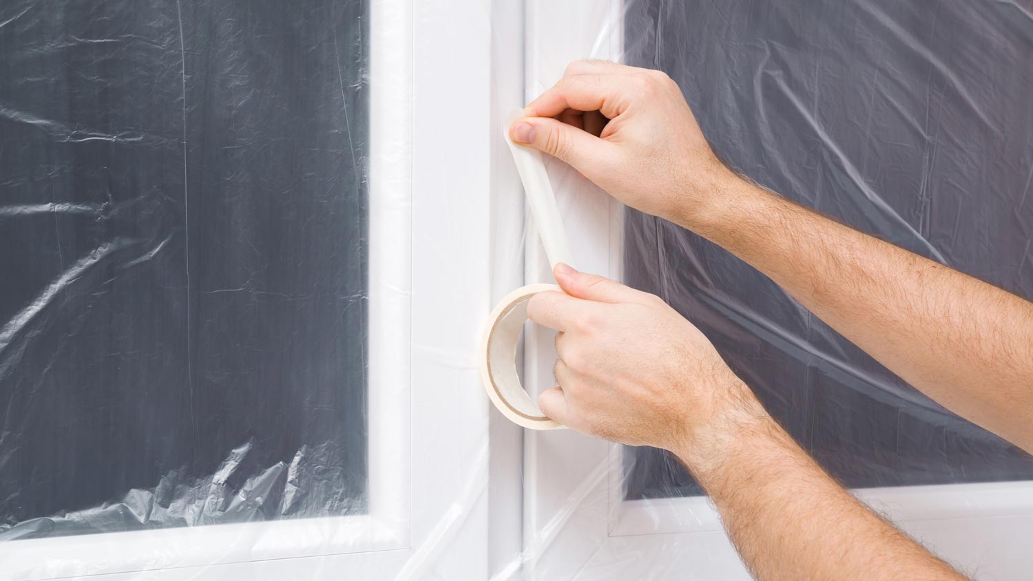 A man covering the windows with plastic wrap