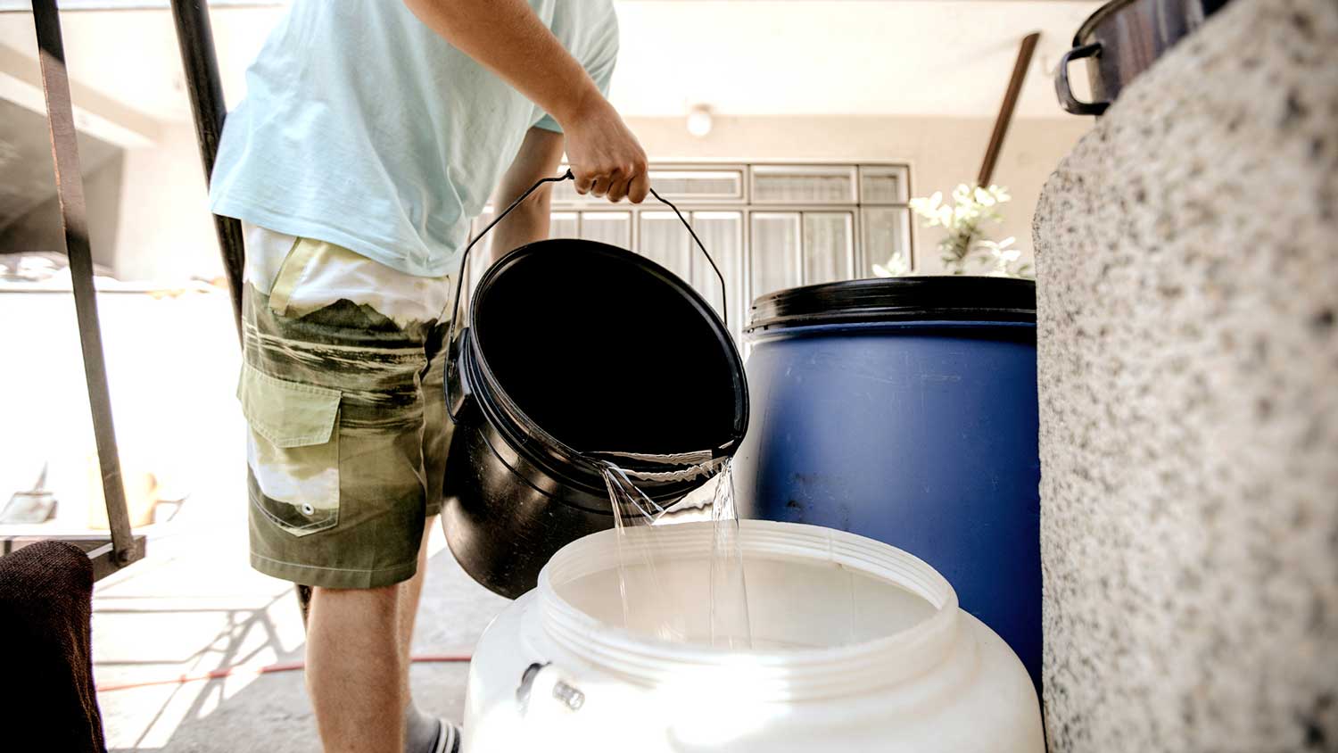 Man using bucket to fill up a barrel with water