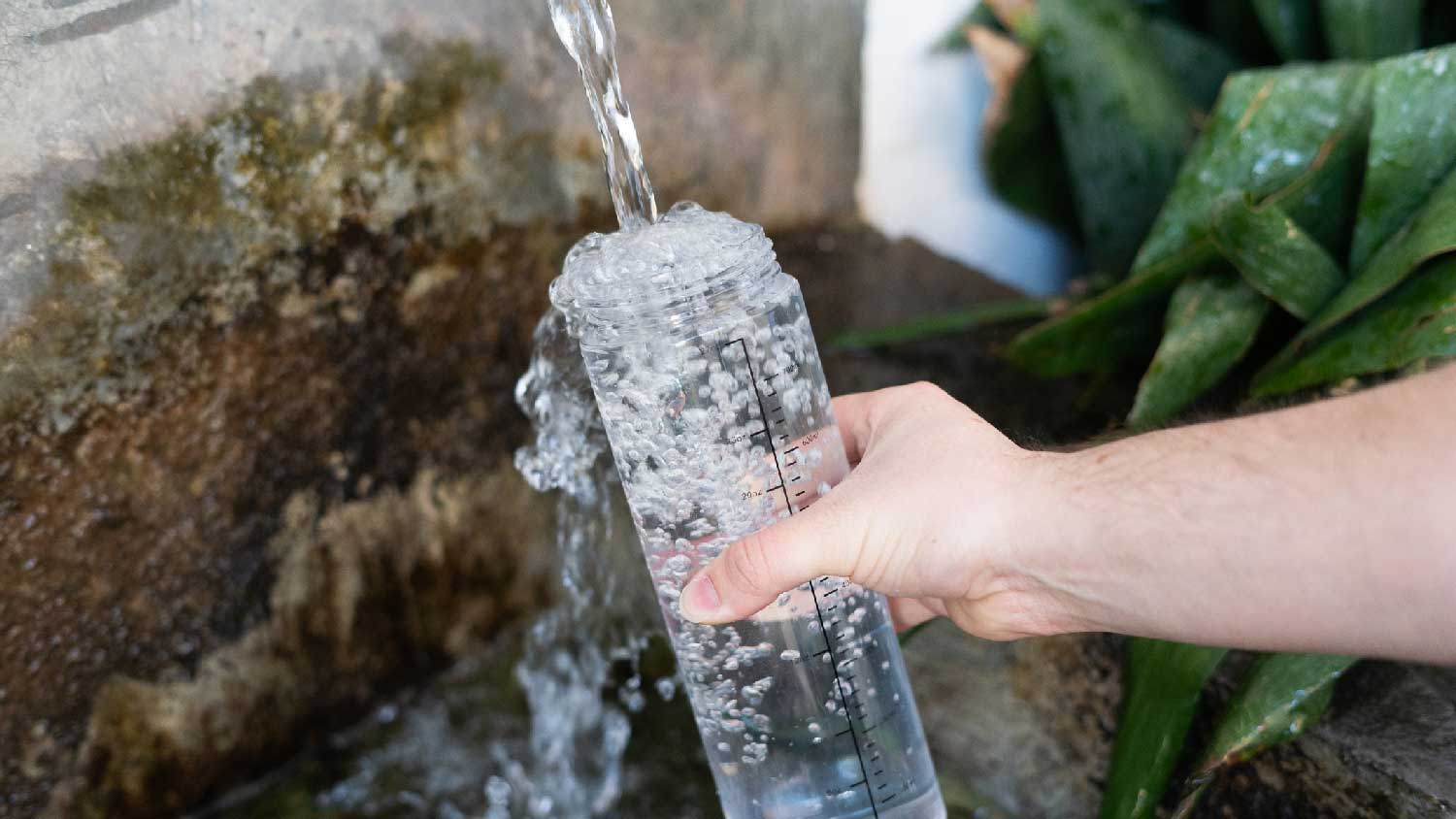 A man filling a glass bottle from a water well