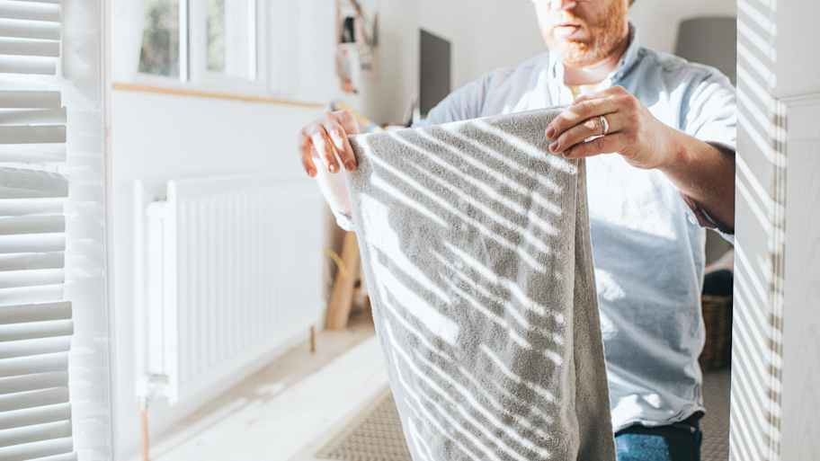Man in a bright room is folding a gray towel