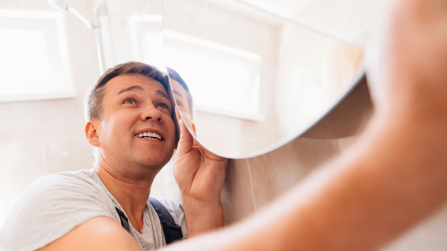 A man hanging a vanity mirror in a bathroom