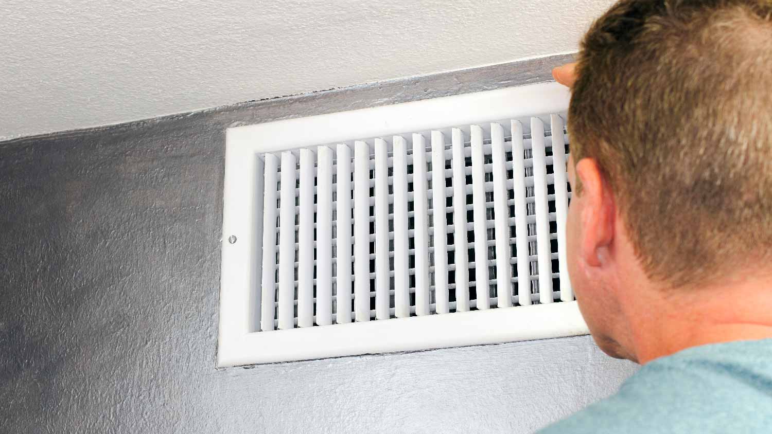 A man inspecting an air vent