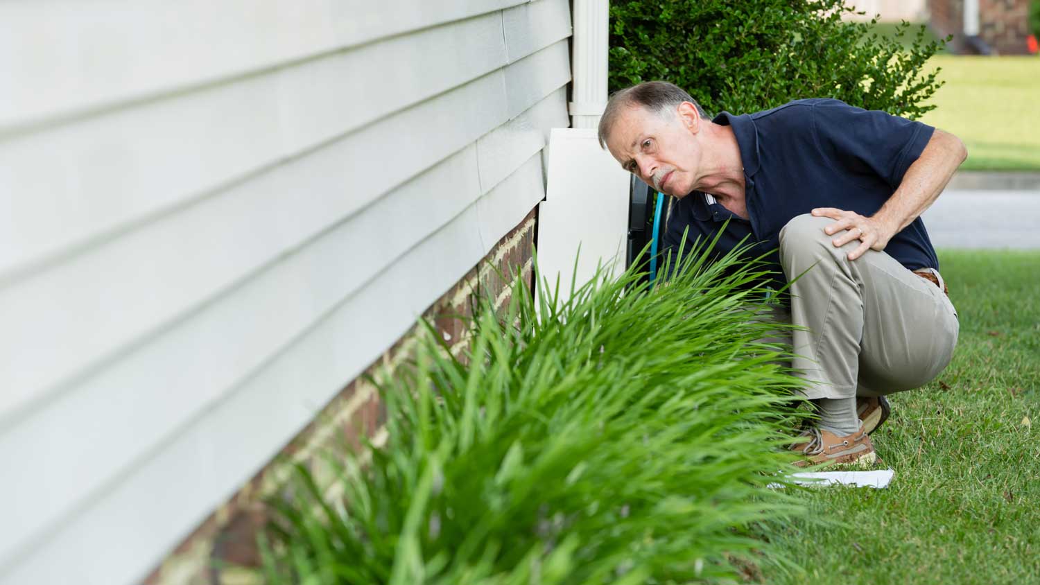 A man inspecting a house’s foundation