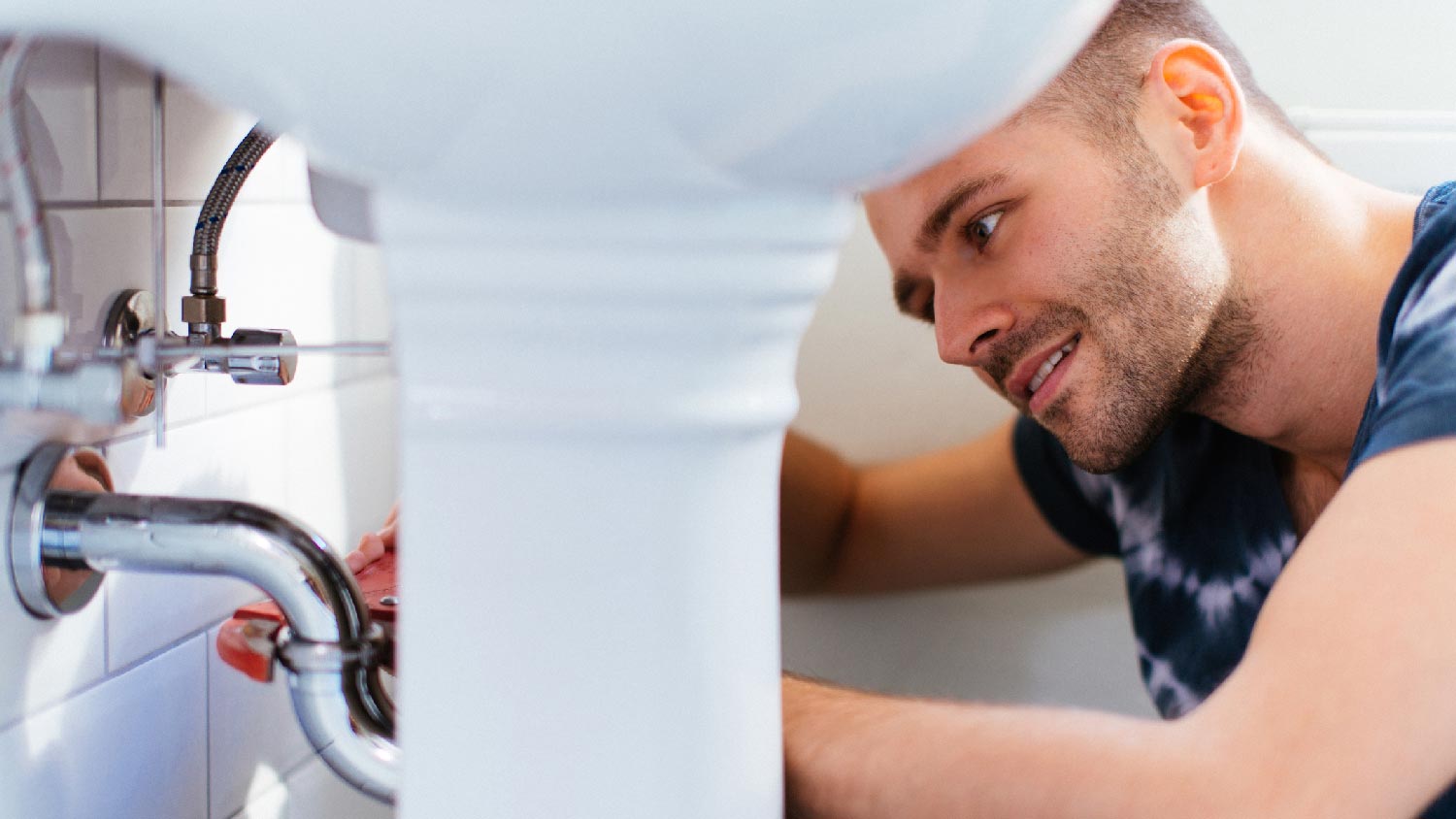 A man inspecting the plumbing in a bathroom