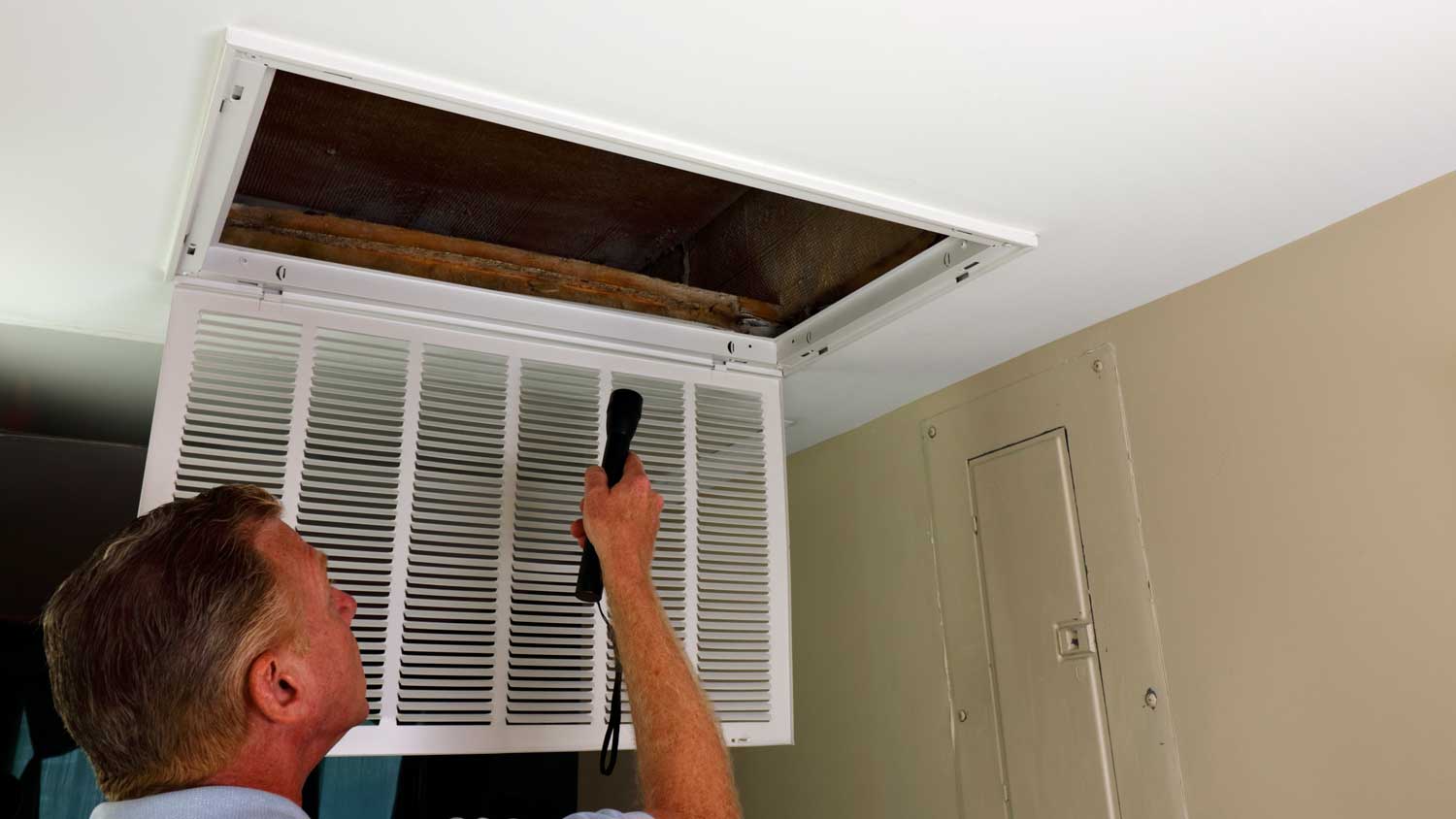 A man holding a flashlight inspecting a vent