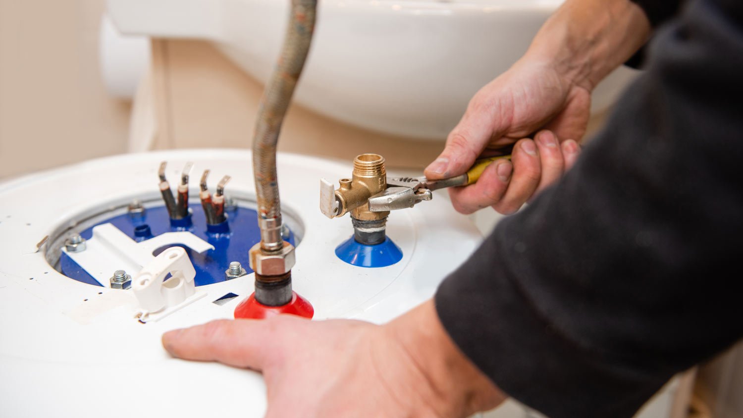 A man installing a water heater using an adjustable wrench