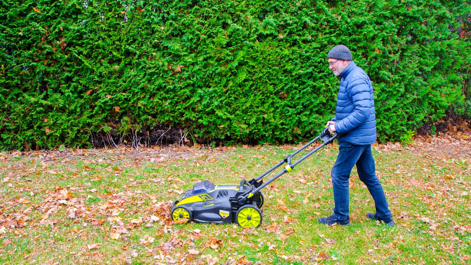 A man using a lawn mower to get rid of autumn leaves