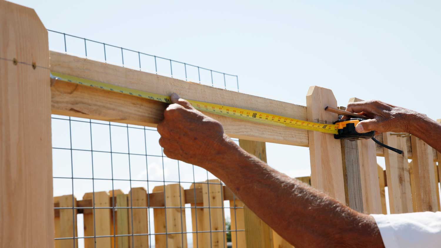 A man measuring a wooden fence