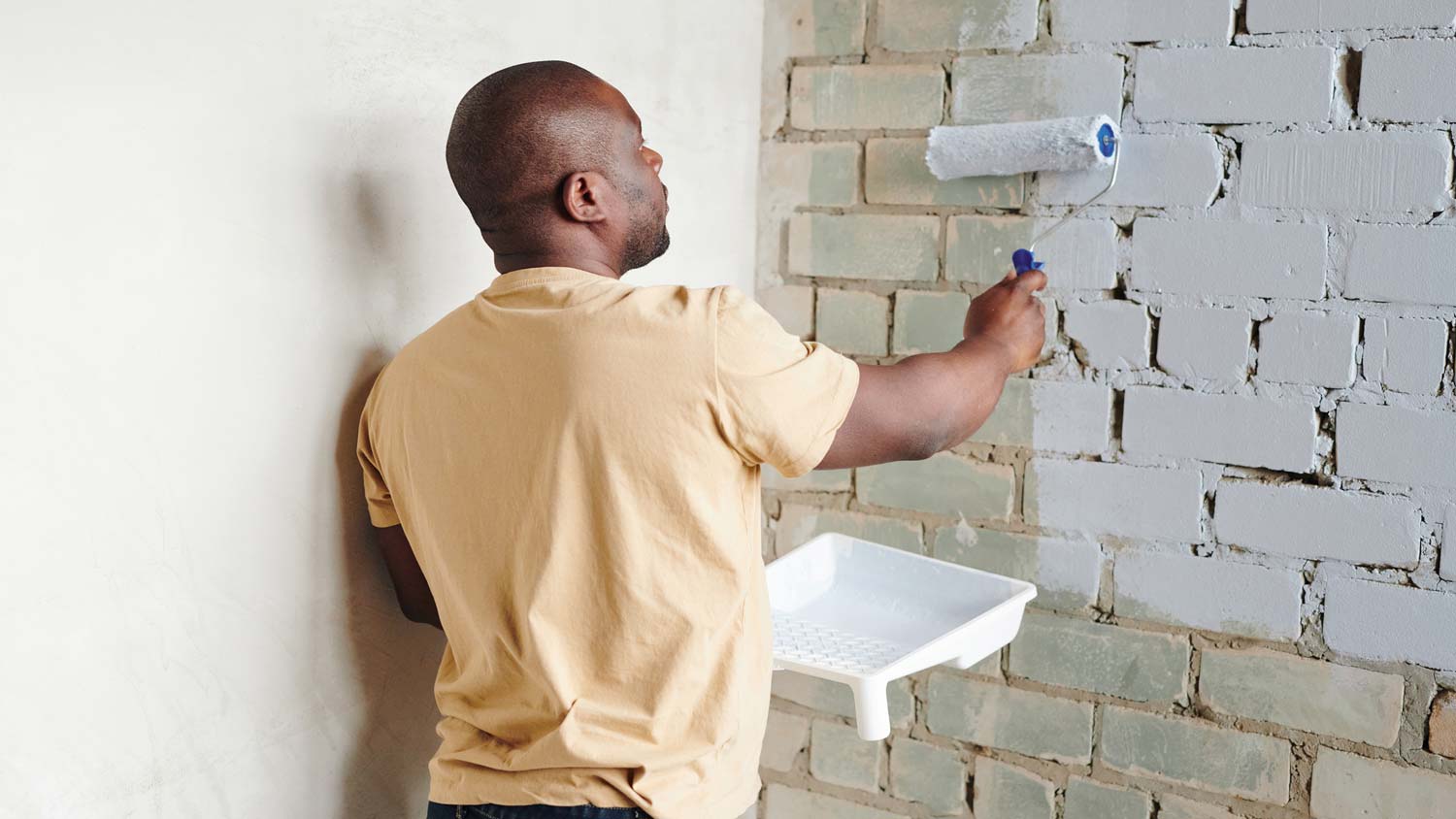 A man painting a brick wall with a roller