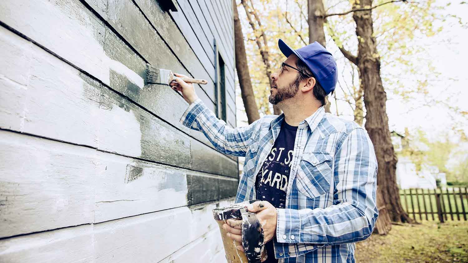 Man painting house siding with a brush