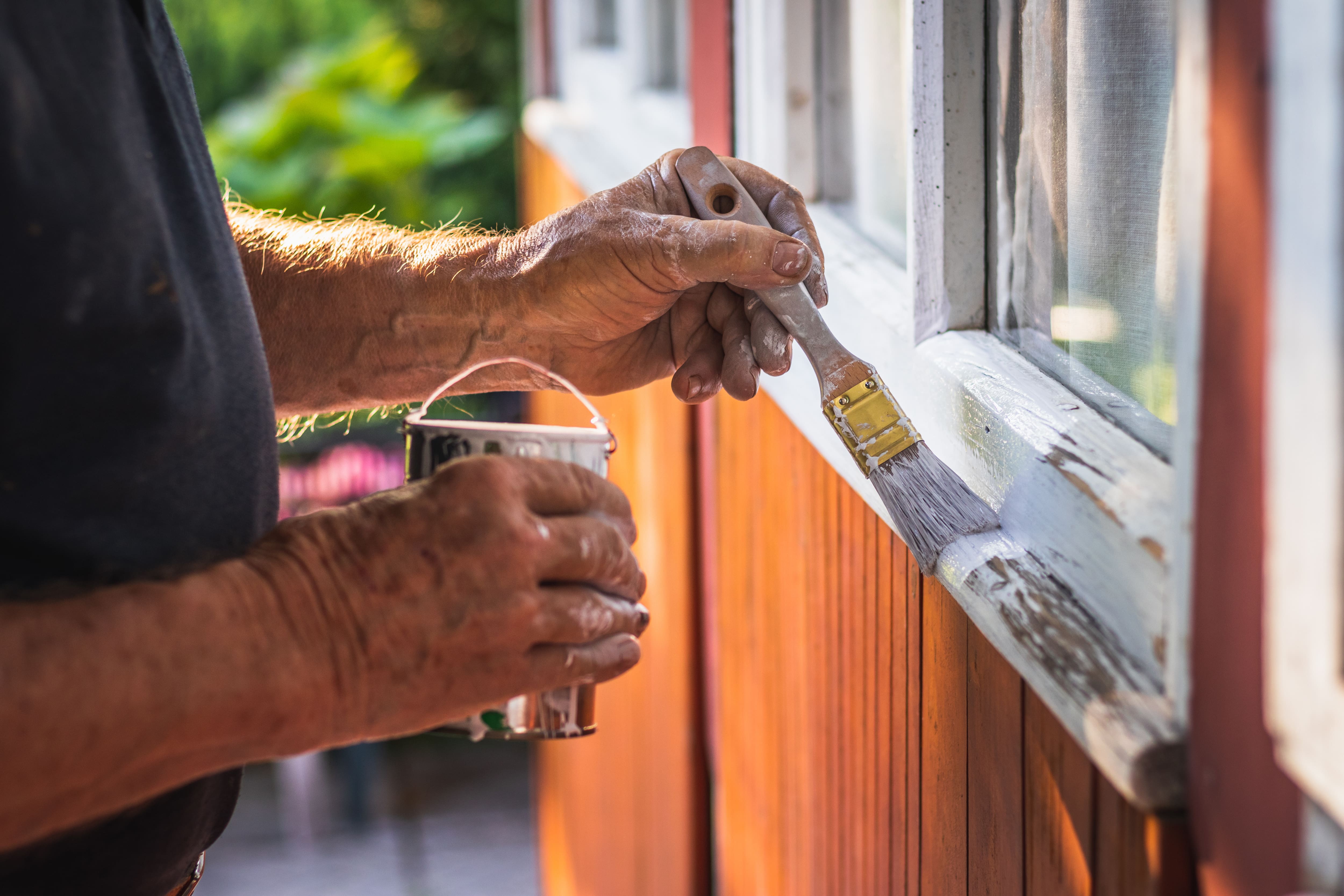 Man painting outdoor window trim with paintbrush