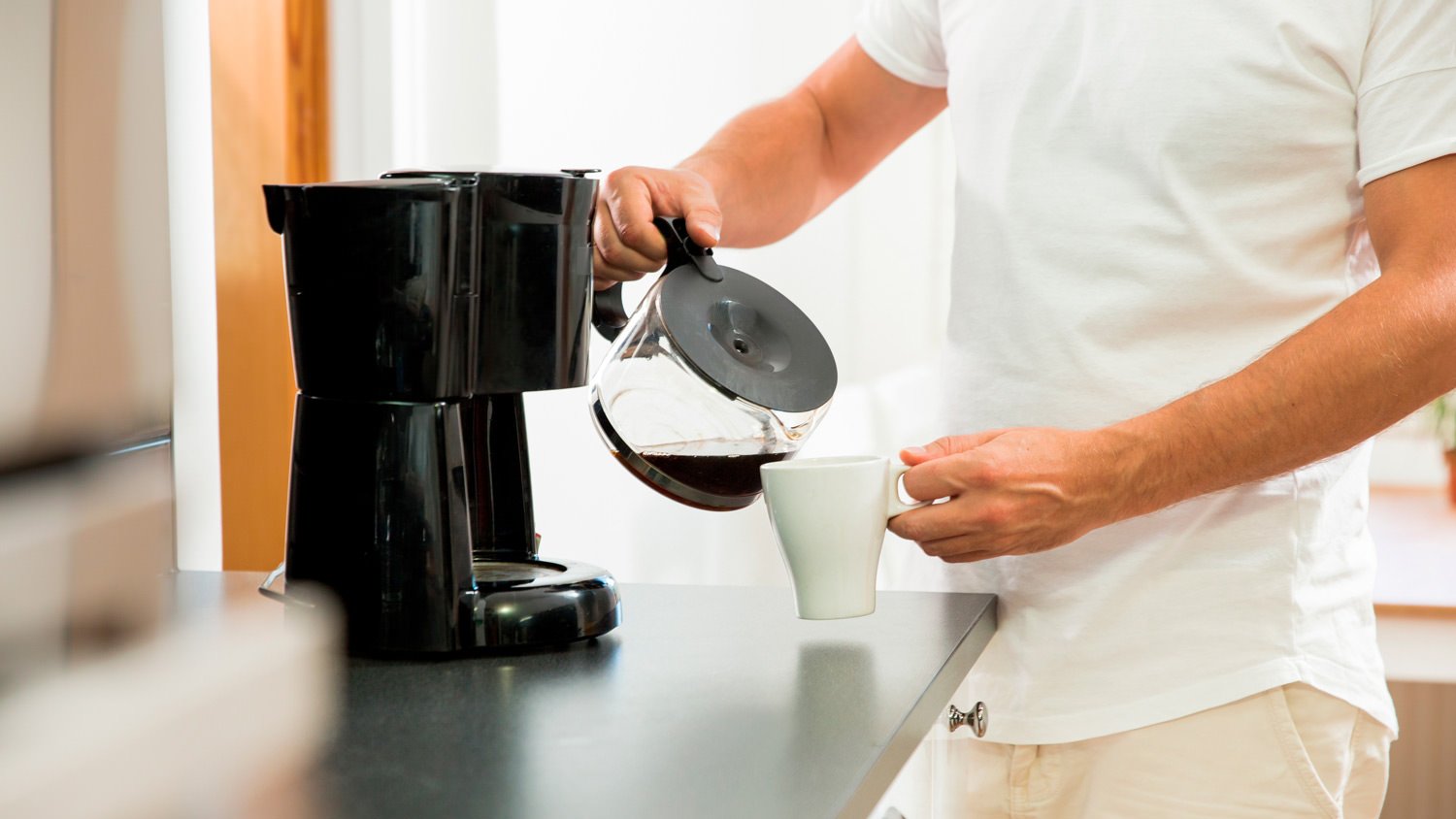 A man pouring coffee from glass pot in the kitchen