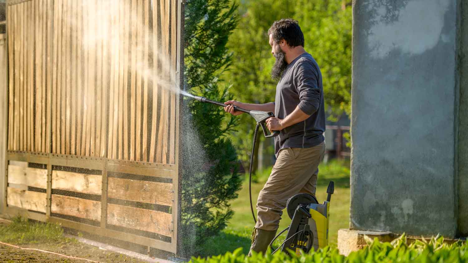 A man power washing a cedar fence