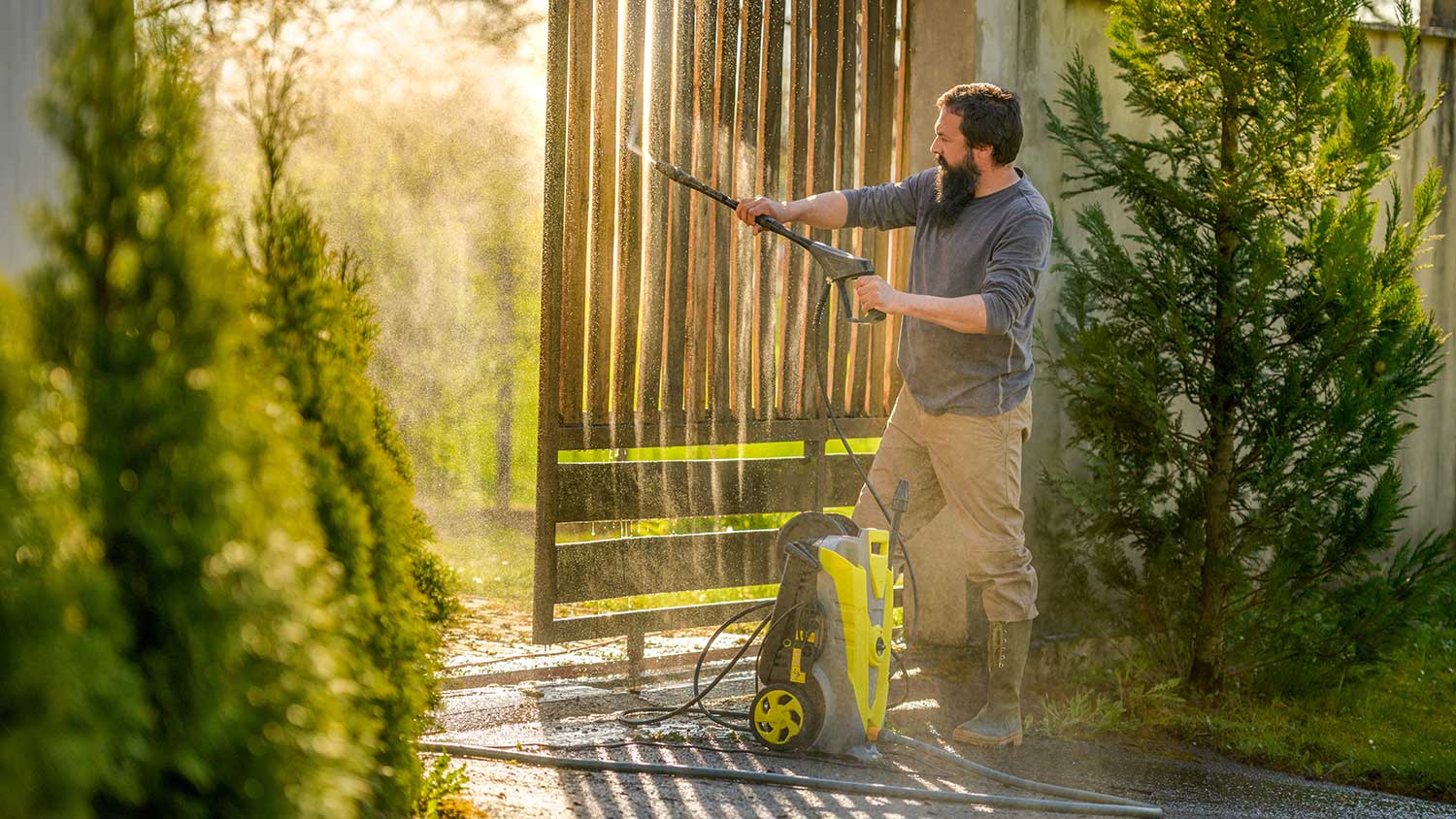 Man cleaning a wooden gate with a power washer