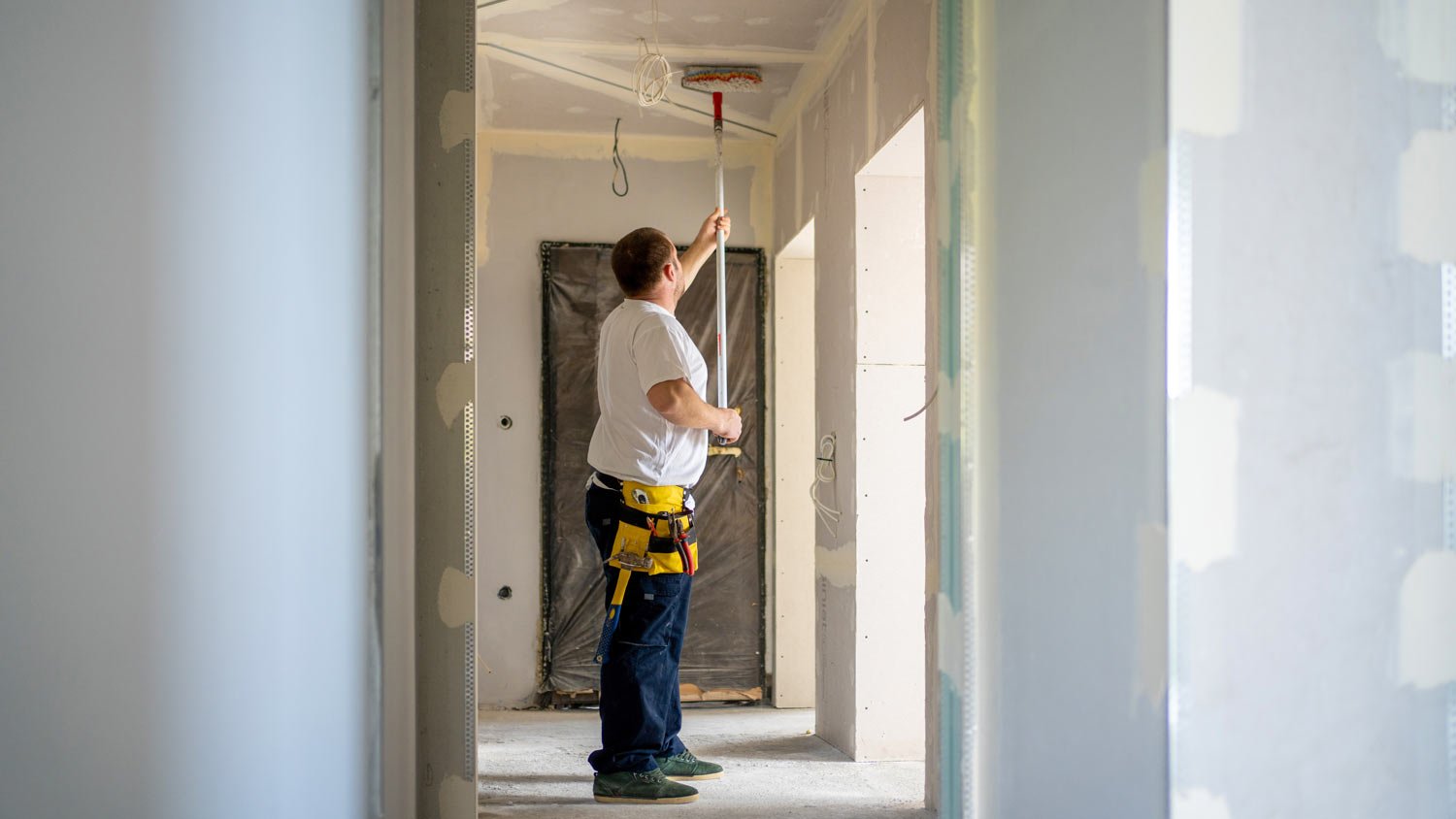 man priming ceiling in home