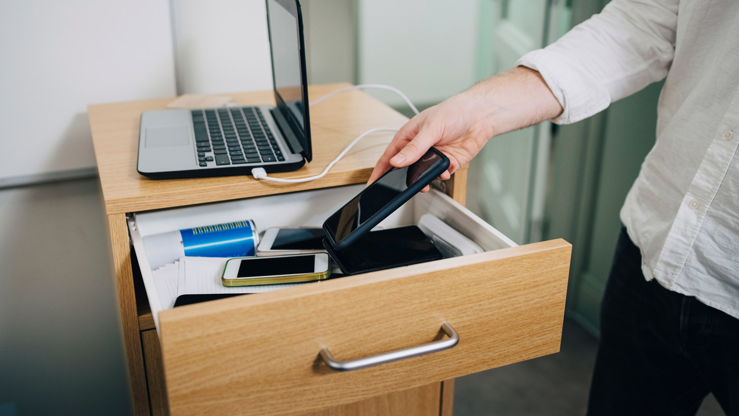 A man putting his phone in the drawer