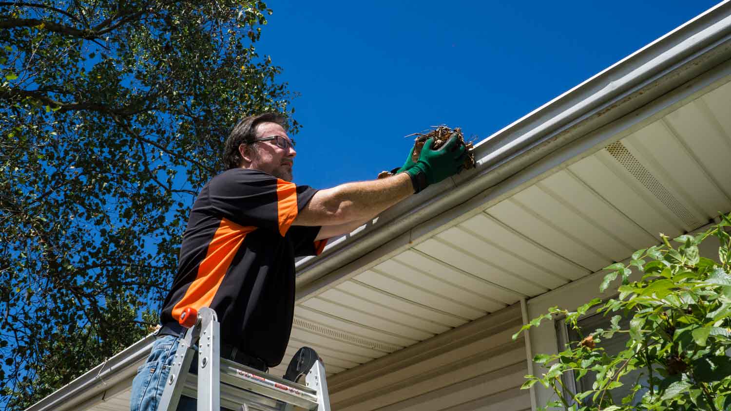 A man removing debris from gutters