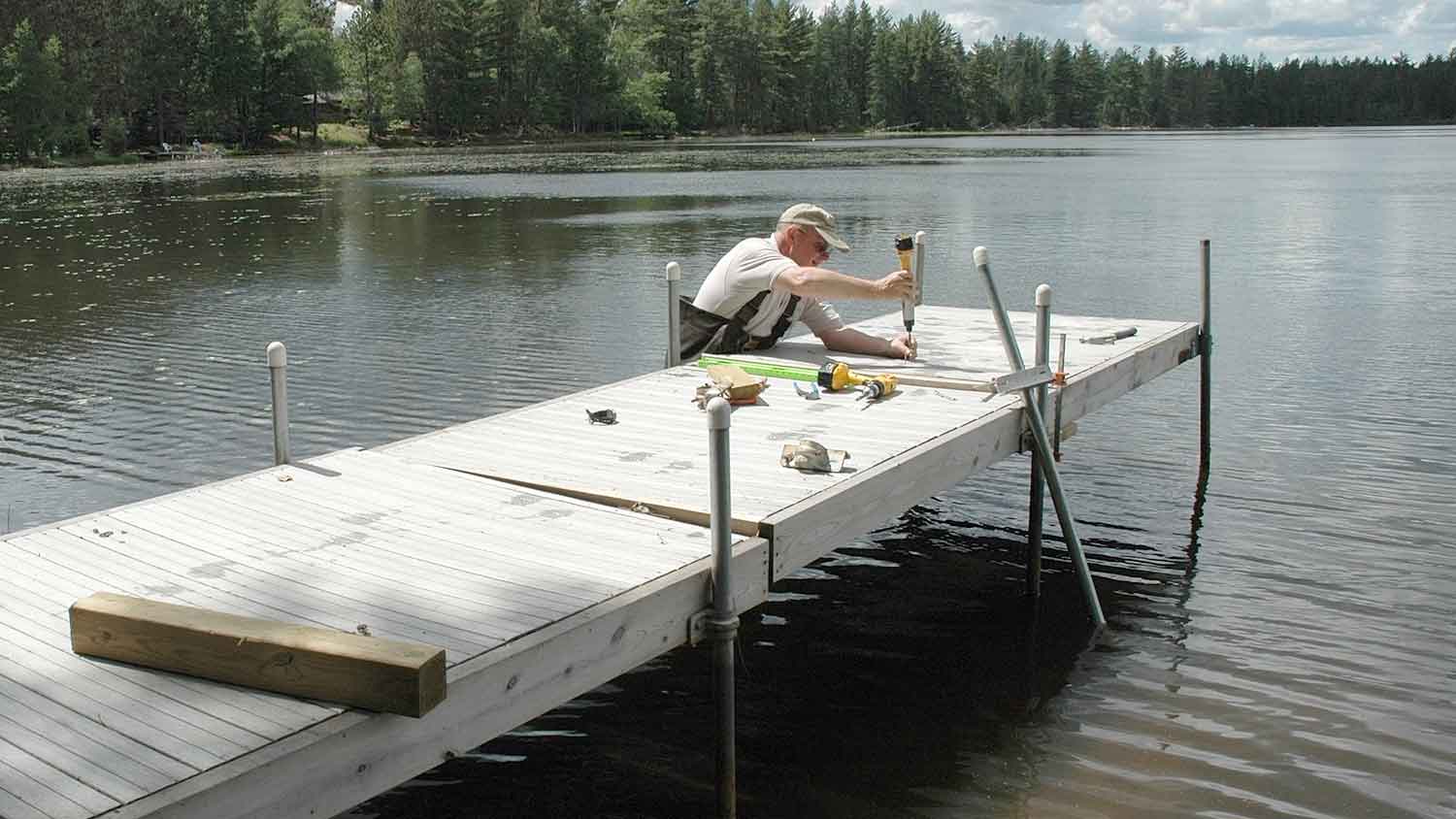 Man standing in the lake repairing a dock board