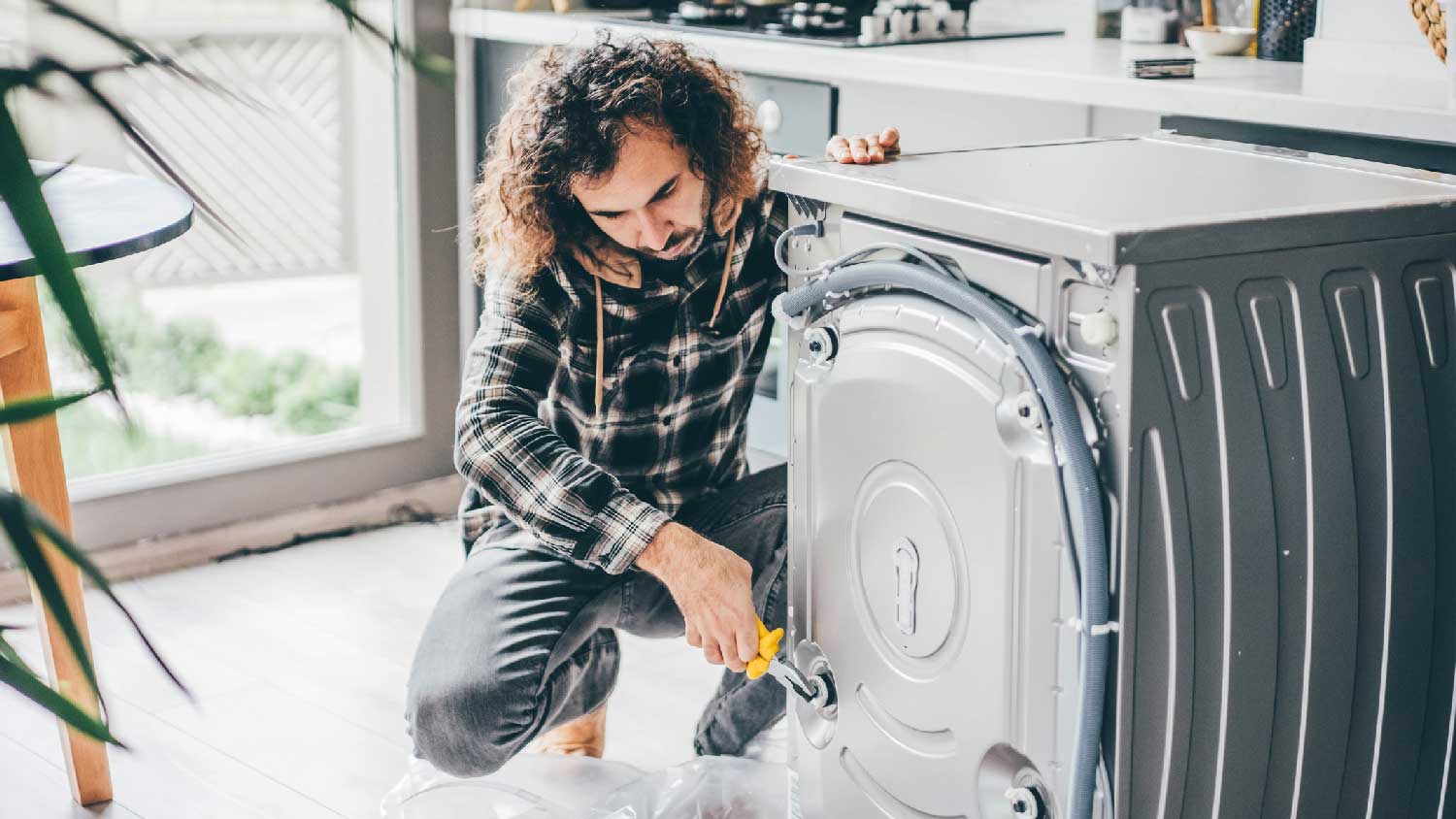 A man repairing a washing machine in the kitchen
