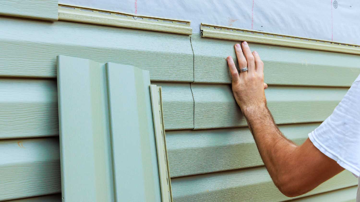 A man replacing the siding of a house 