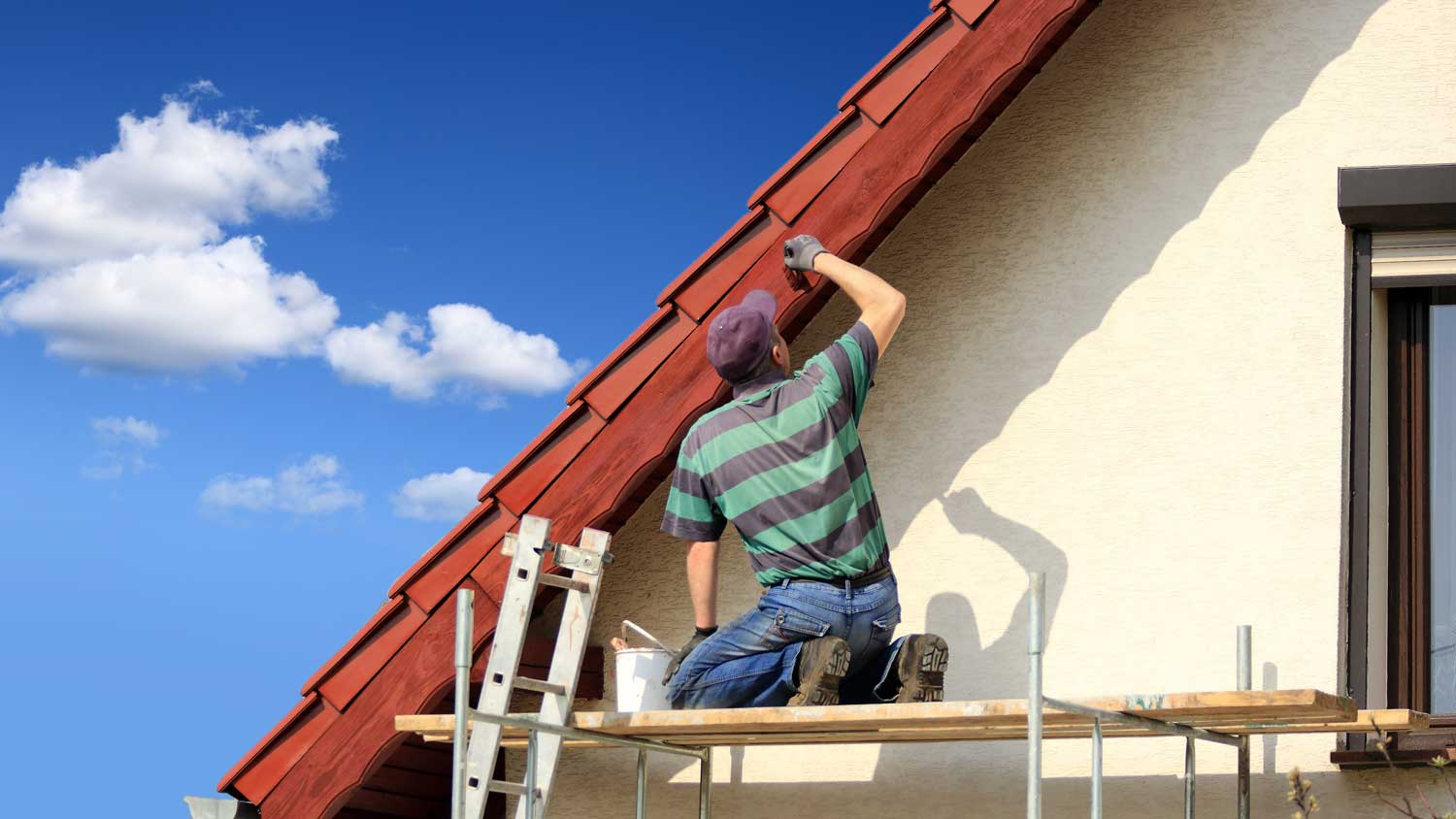 A man on scaffolding painting a roof