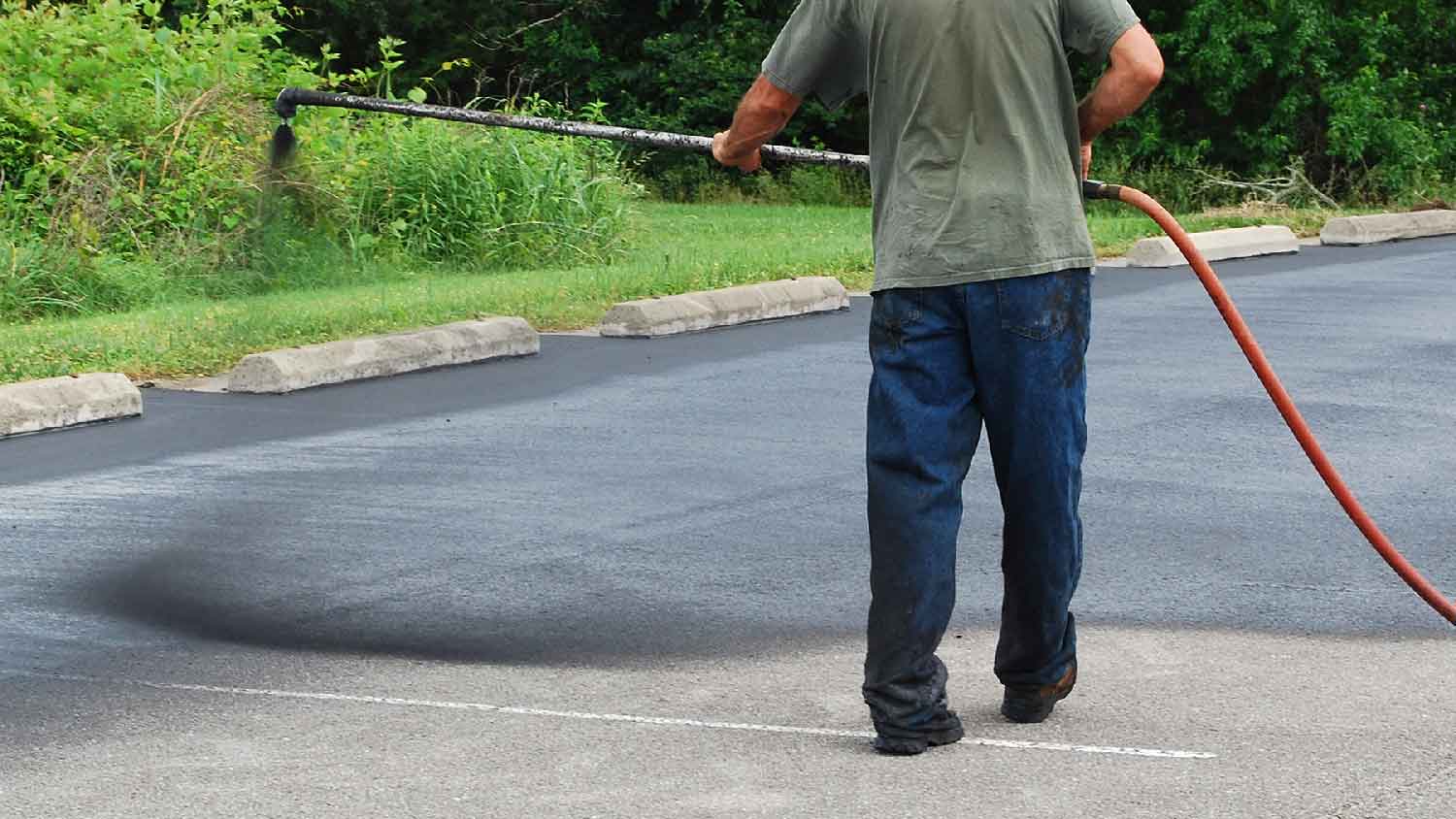 A man sealcoating an asphalt driveway 