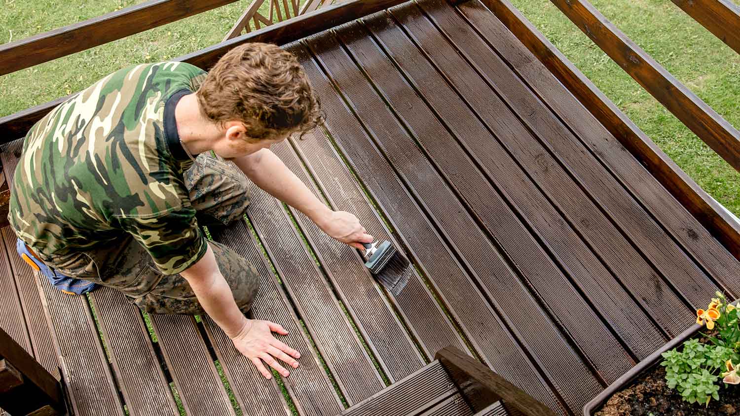 Man using a brush to stain a deck in the yard