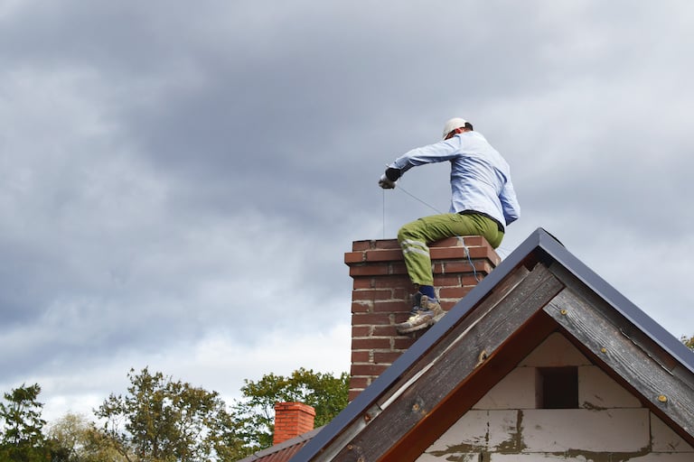 man sweeping chimney on top of house