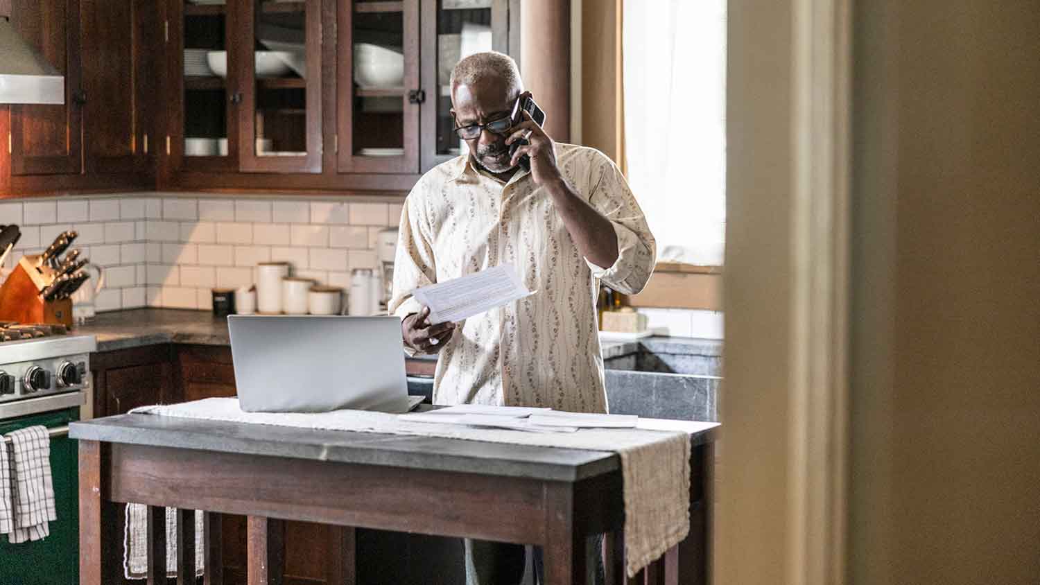 Man in the kitchen using his phone and holding a piece of paper