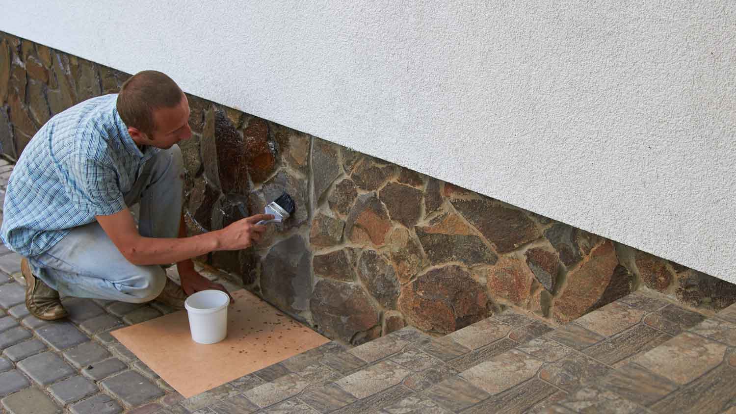 A man varnishing a house’s stone foundation