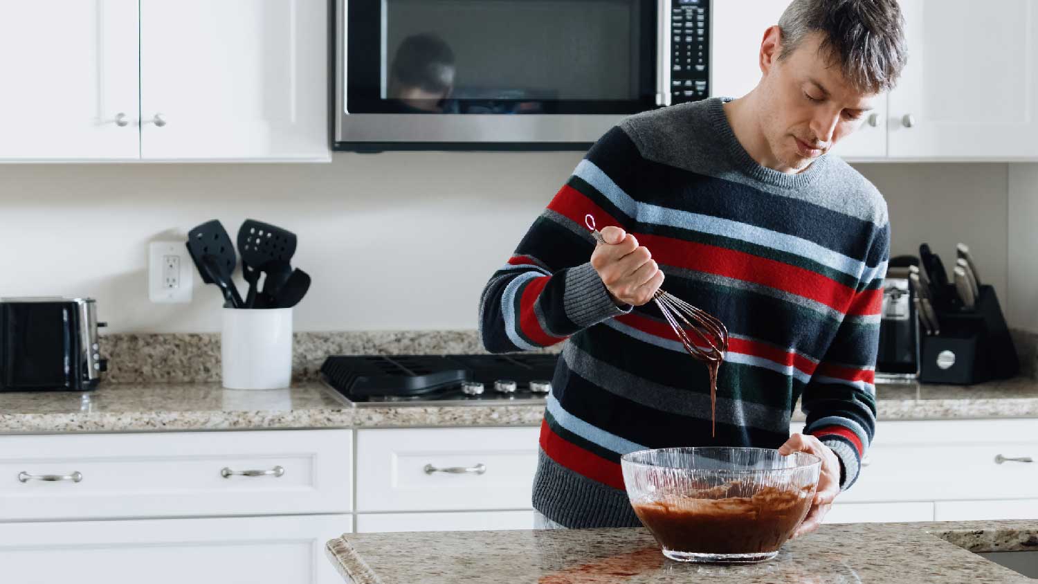 A man whisking chocolate batter on a granite countertop