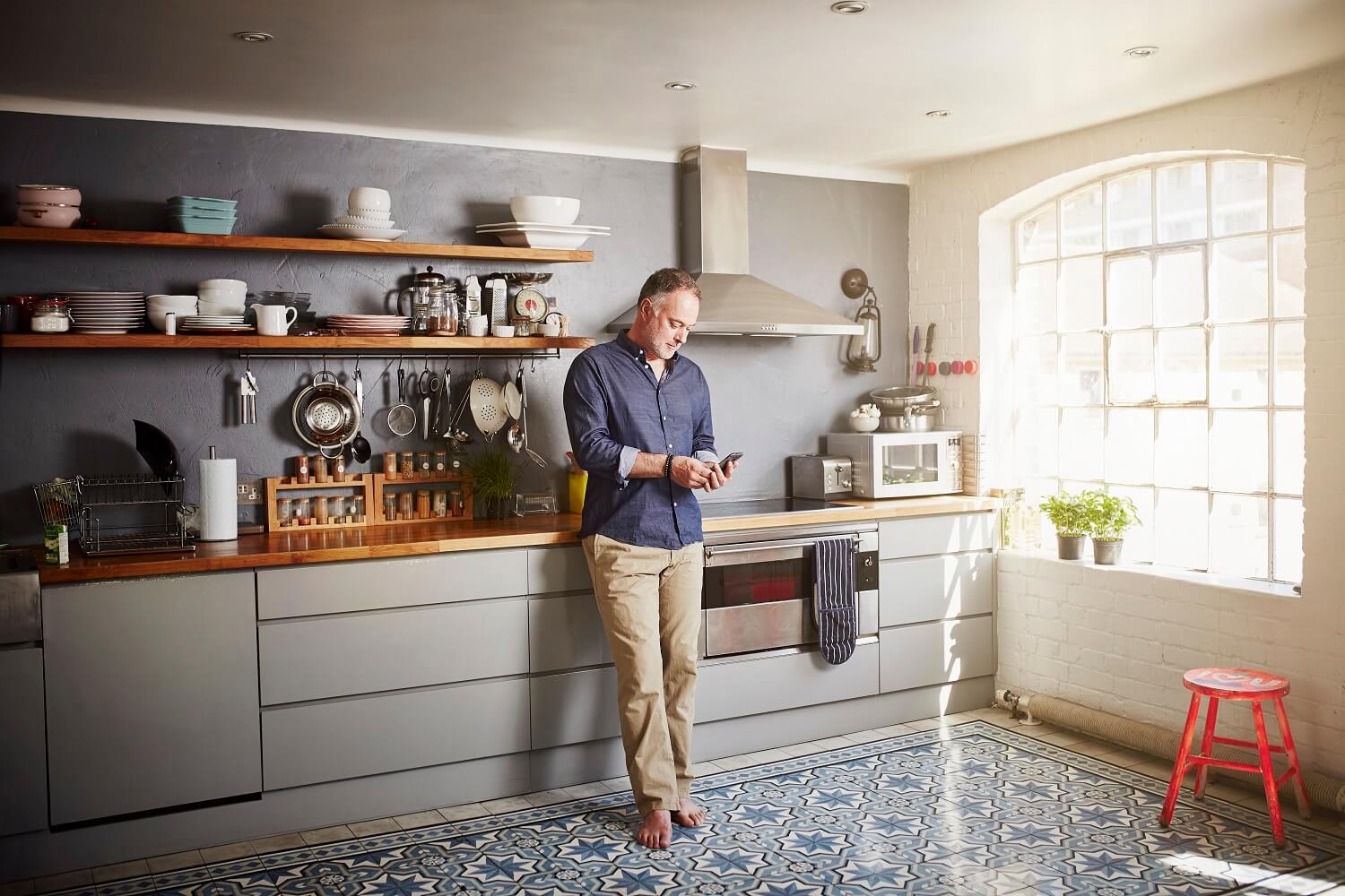 man stands in urban, modern kitchen with his phone