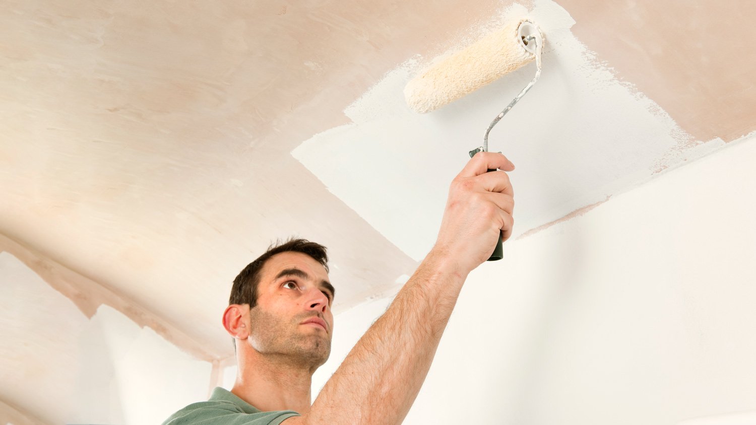 Man painting a newly plastered ceiling white, using a roller