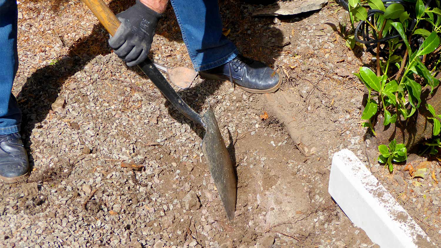 Man digging hole in stone with shovel in garden