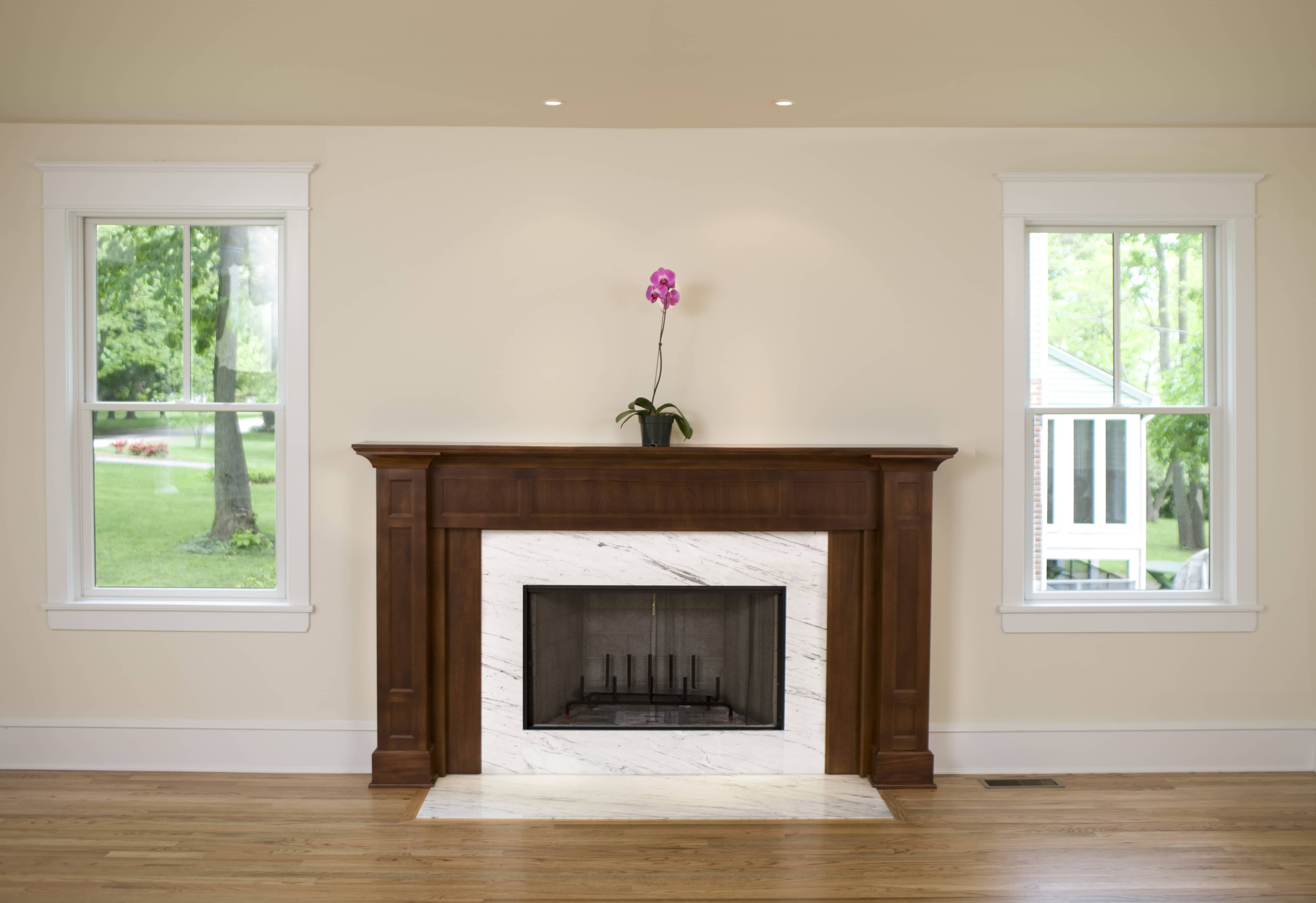 White marble fireplace with dark brown wood mantel holding orchid plant