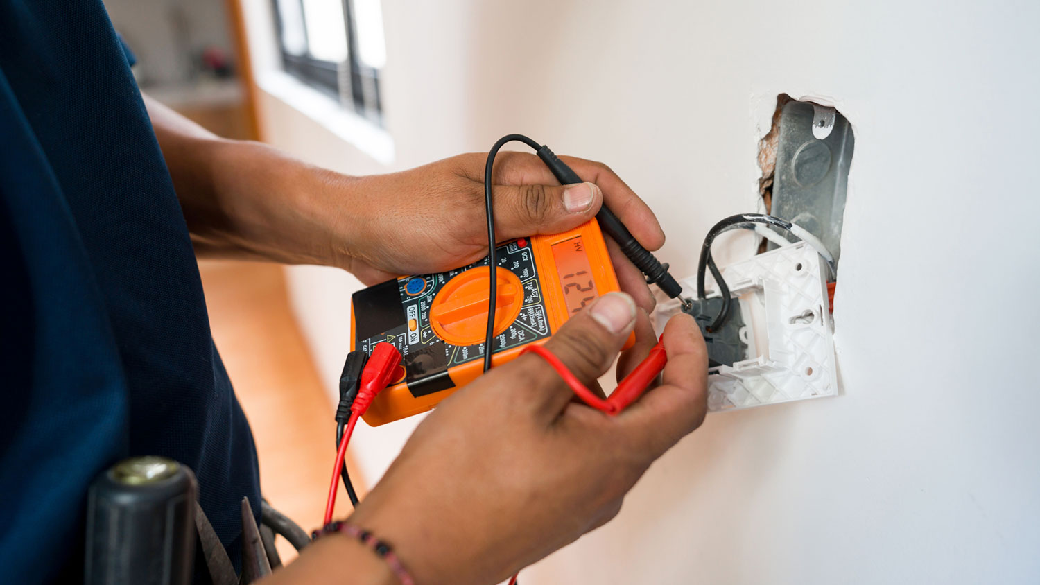 Electrician measuring electrical voltage in a wall outlet