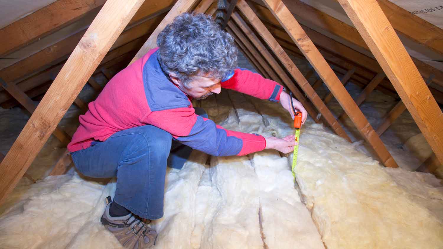 Homeowner in the attic measuring insulation depth