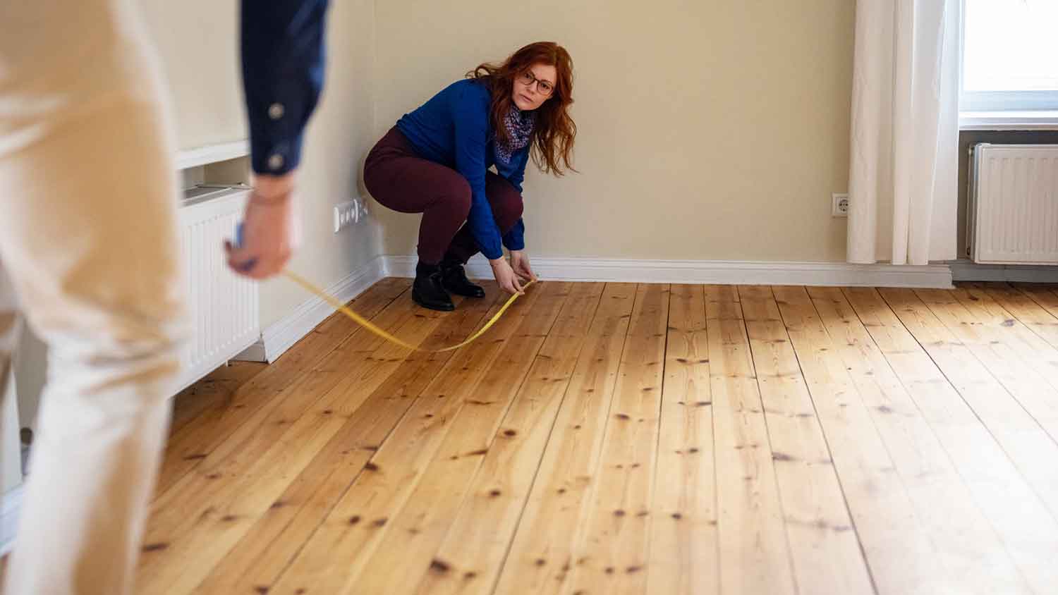 A couple using a measuring tape to measure the living room floor