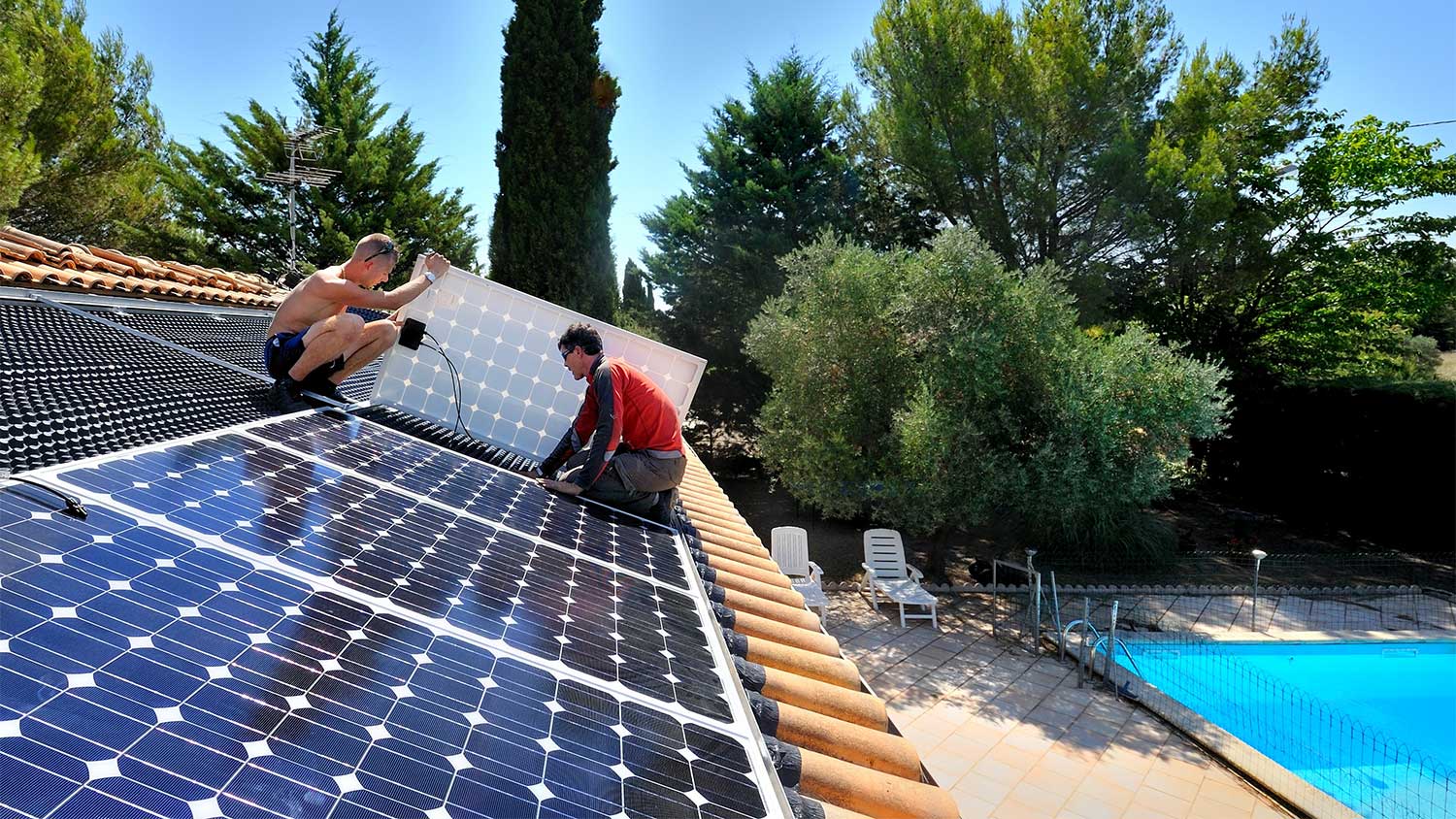 two workers installing solar panels on a house roof