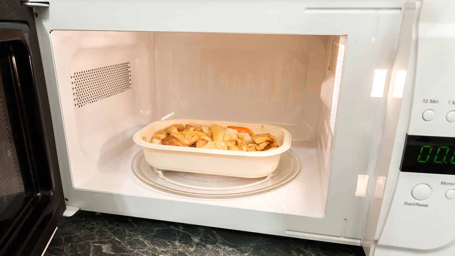 Tray with food inside of a microwave with the door open 