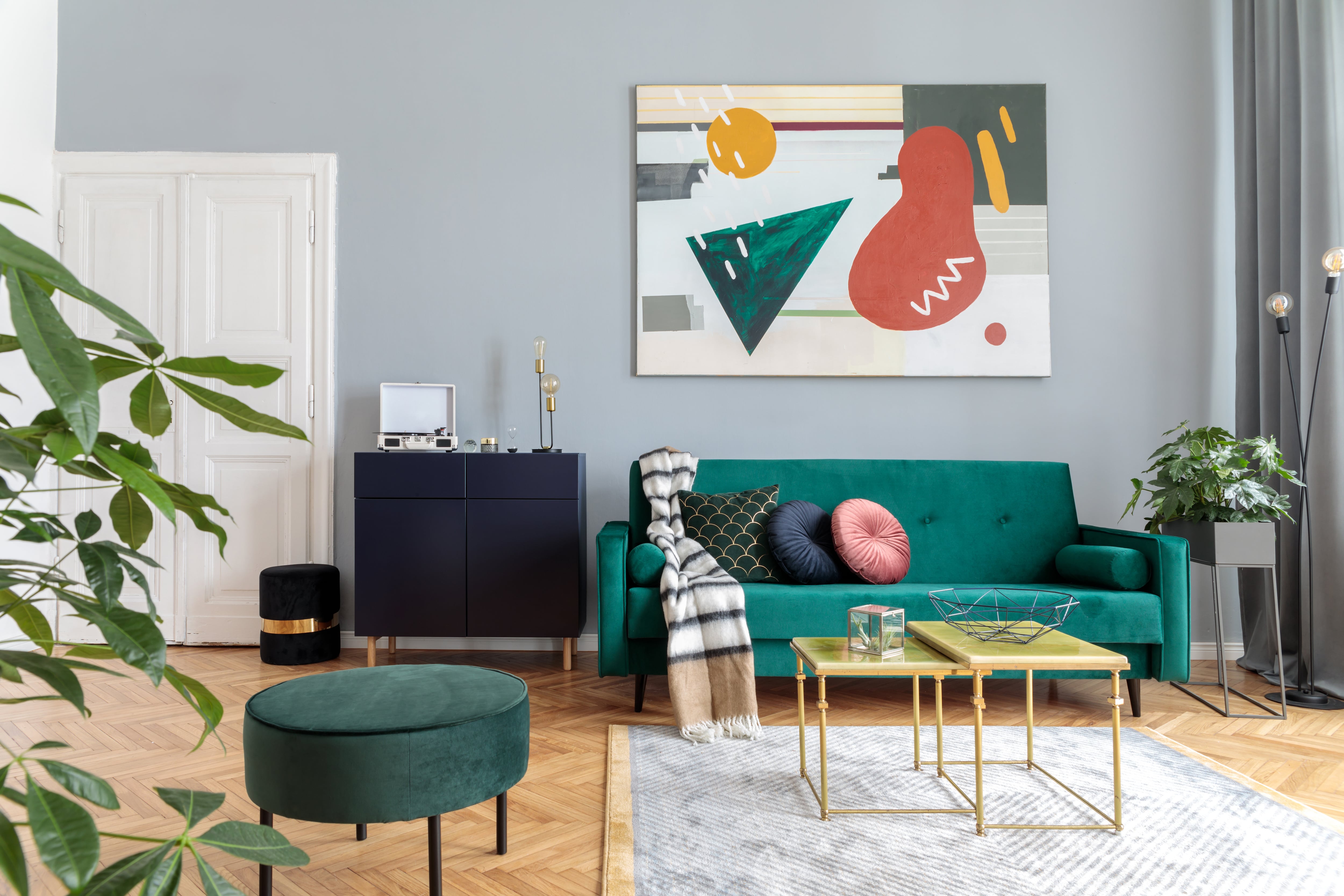 Mid-century modern living room with a green velvet sofa, matching ottoman, and vibrant abstract artwork
