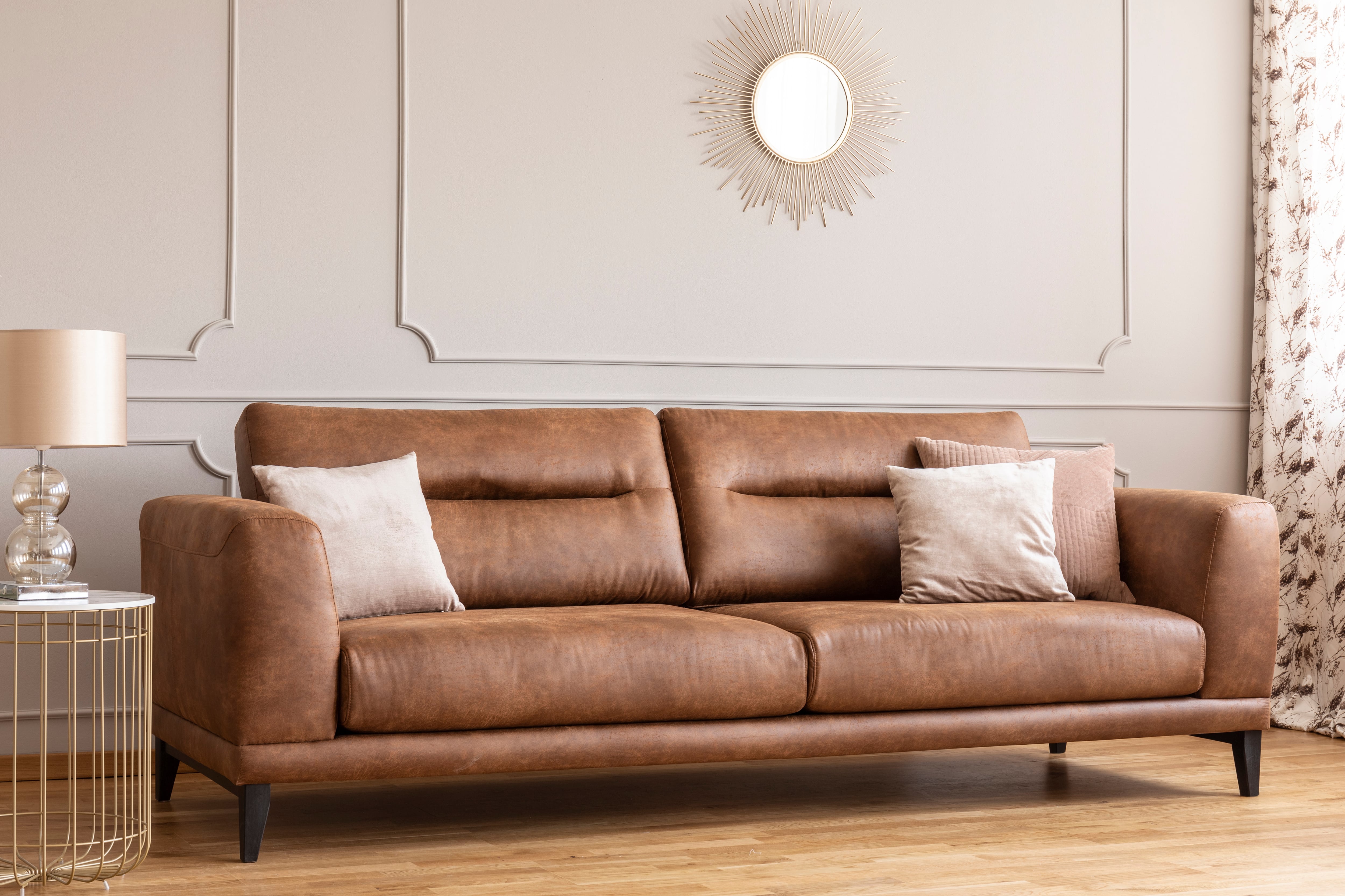 Leather sofa with accent pillows sits next to a metal side table and sunburst mirror overhead