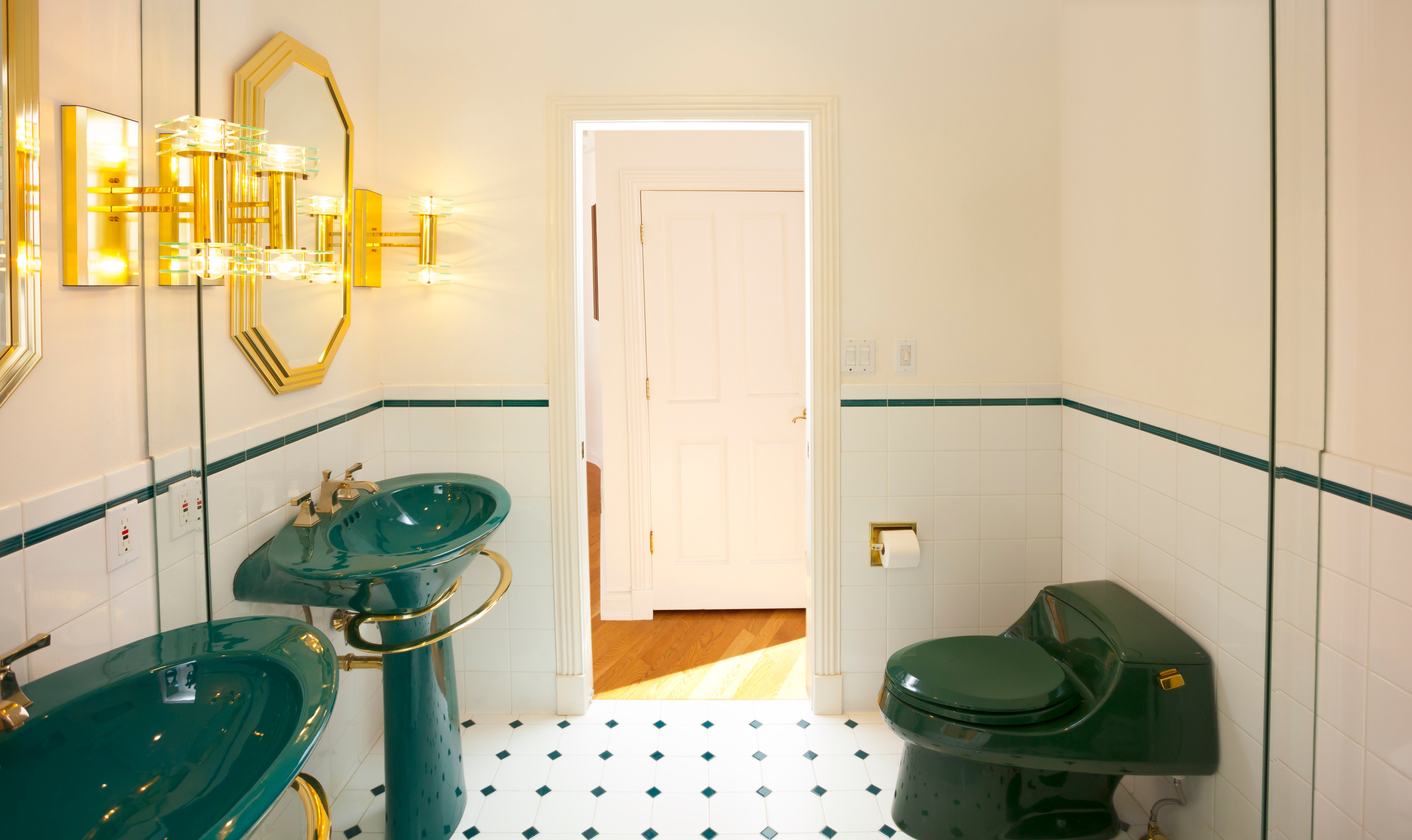 Bathroom with green sink and toilet, gold metal accents, black-and-white tile floors, and a mirror covering the back wall