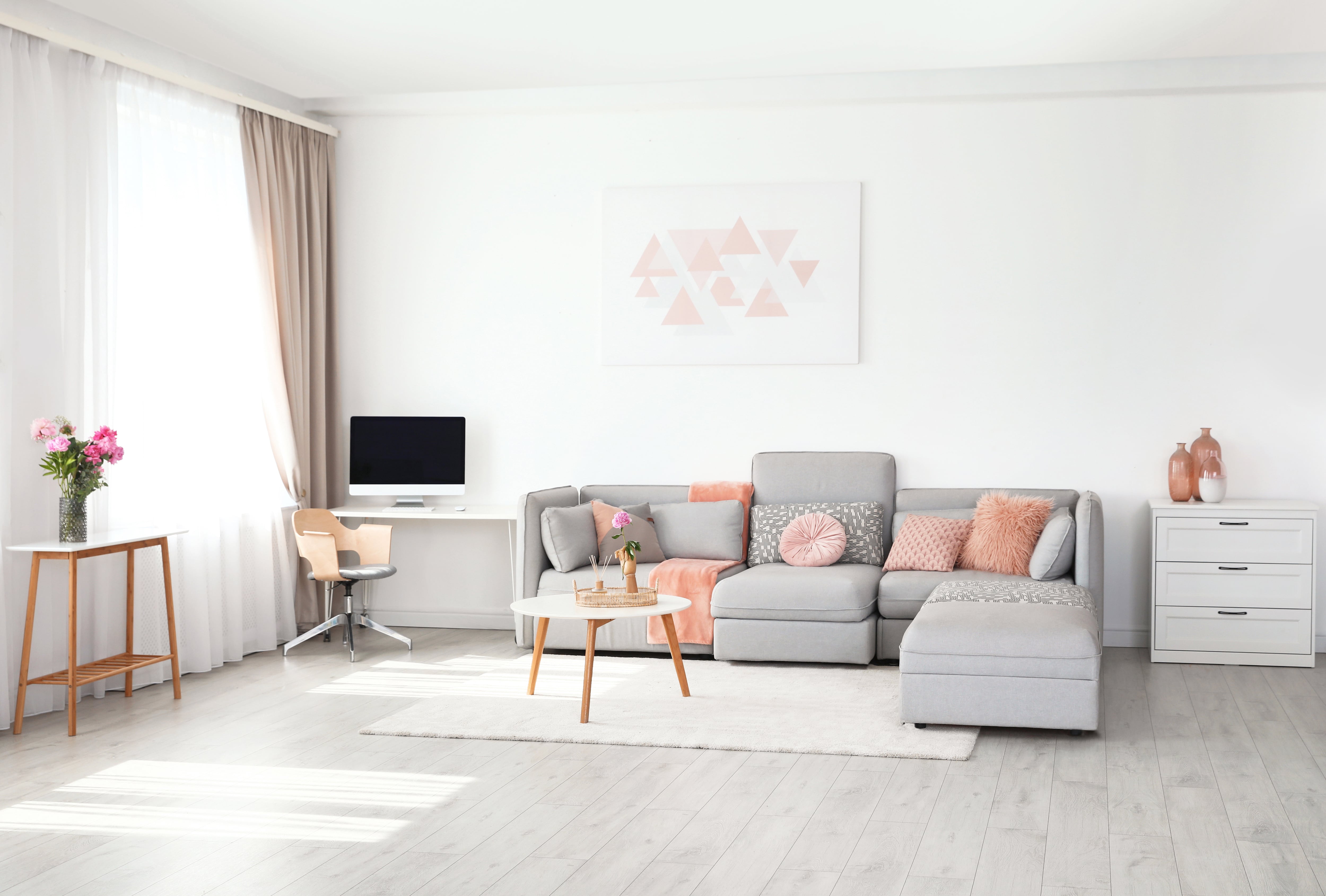 A modern white living room with blush accents and a small desk