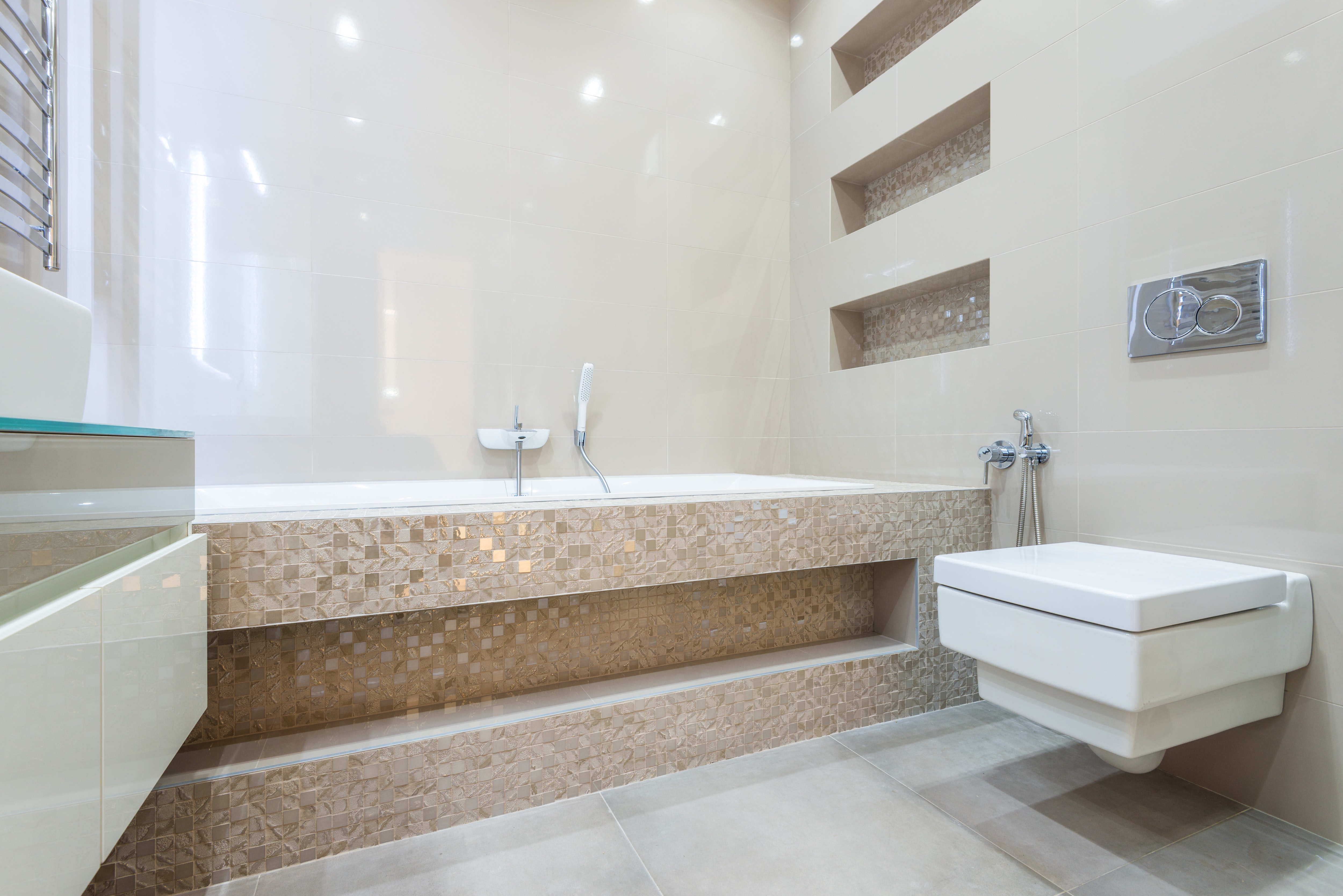 Bathroom with brown mosaic tile tub, wall-hung toilet, and built-in mosaic shower shelves