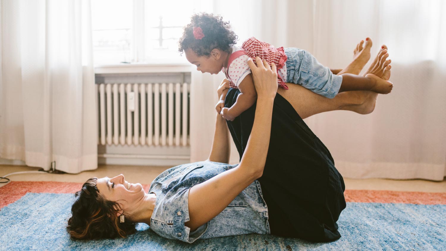 Mother lifting daughter while lying on carpet at home